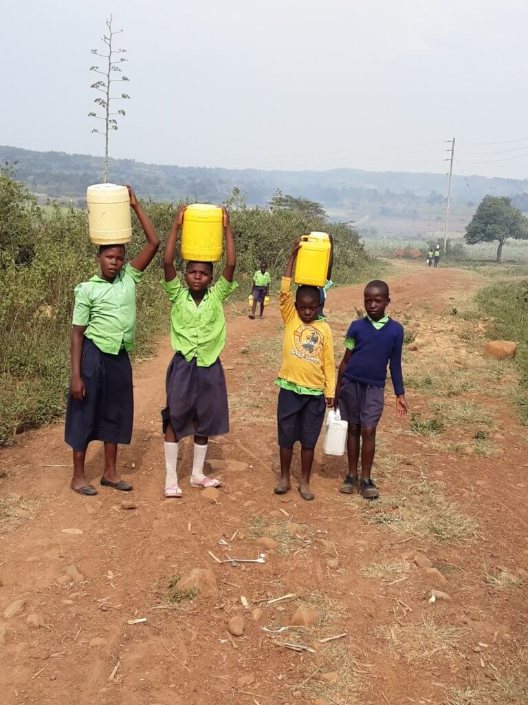 Collecting water: four children in school uniforms with yellow jerry cans on their heads