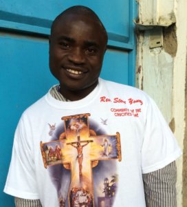 An update to the story: Simon Wanjala in front of a blue door with a big smile