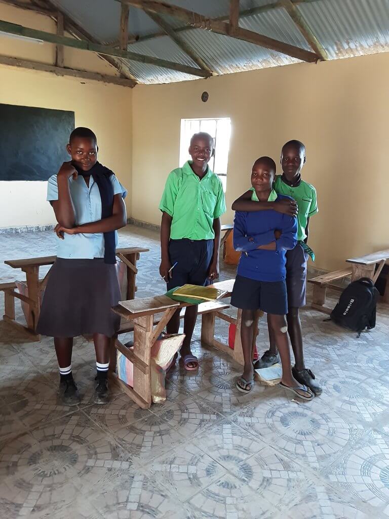 Several young adults at the Miruya Primary School standing in their new classroom, dressed in  green shirts and blue shorts. 
