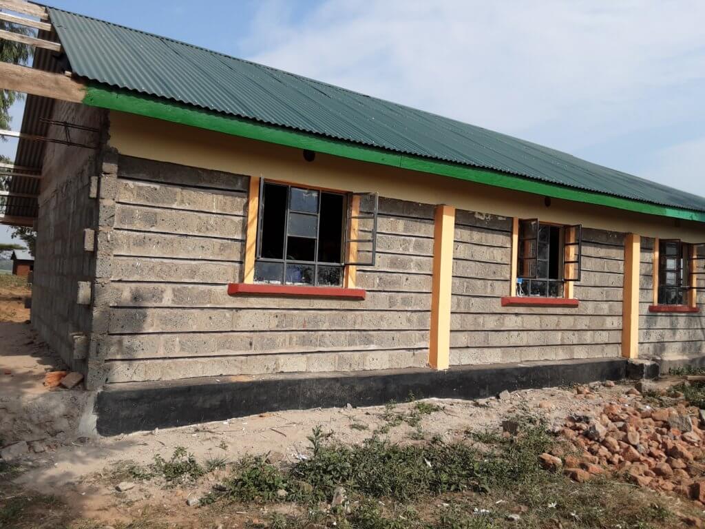 Outside the new stone classroom with a green metal roof and orange casings around the windows