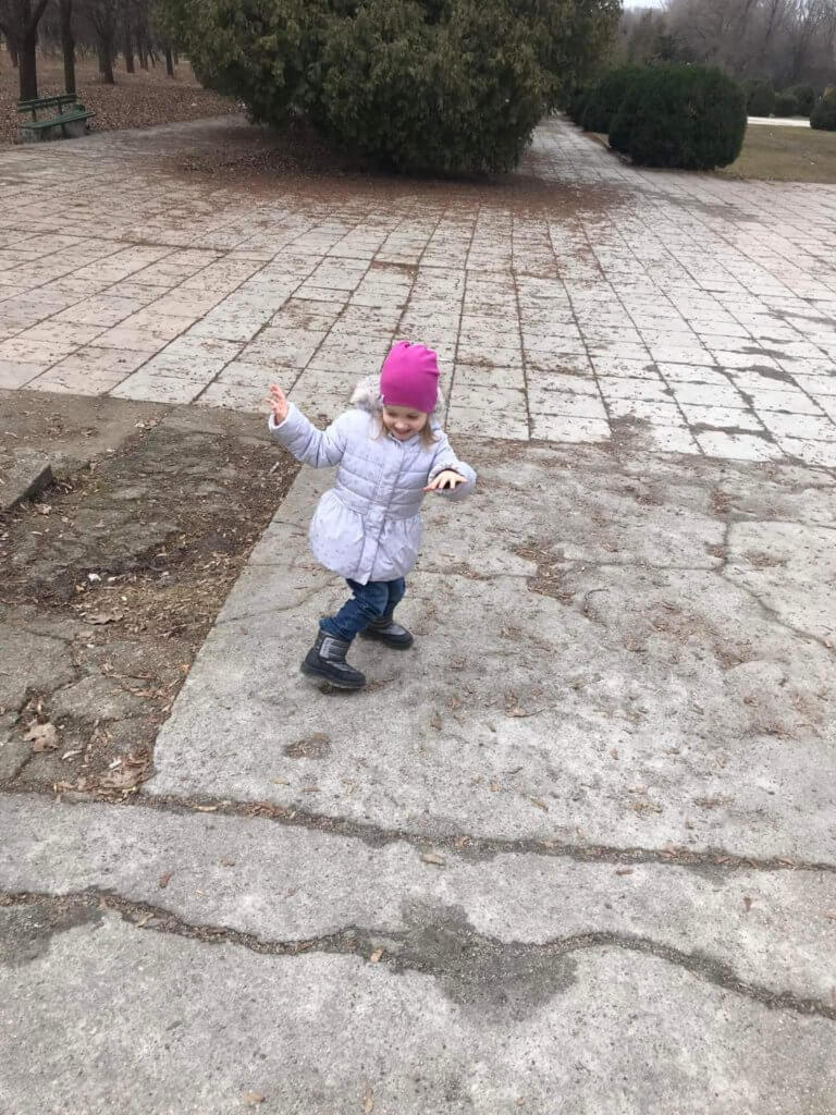 Little Ukrainian child wearing a pink hat dances on the gray bricks in a park