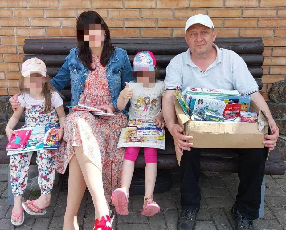 Good News: A man sits with two young girls and their mother on a bench with donated art supplies.