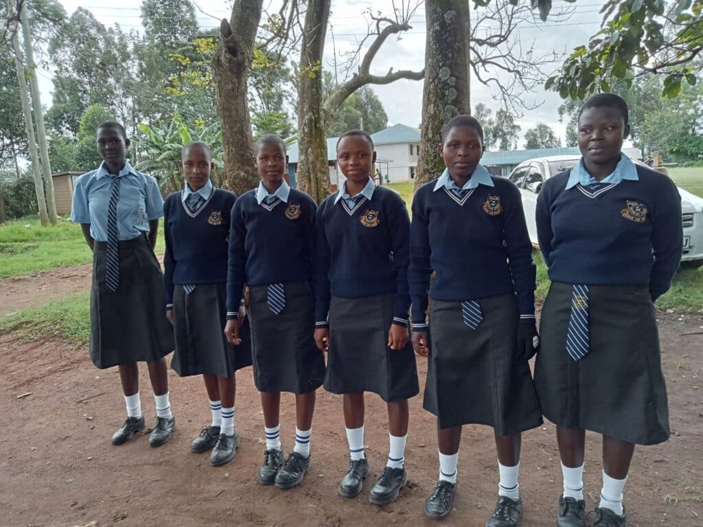Six Kenyan female high school girls wearing blue sweaters, skirts and ties: new school uniforms