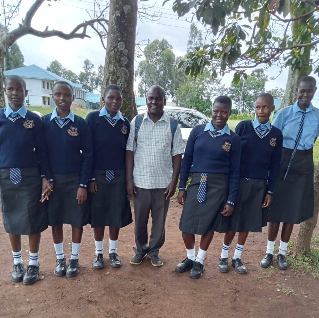 Six kenyan girls in new school uniform standing outside with a man